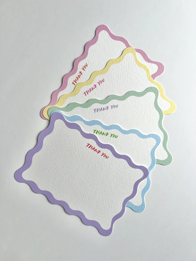 A fan of five wavy edged notecards with colourful borders and Thank You written at the top of each notecard