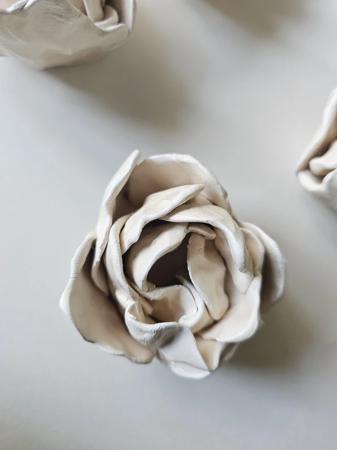 hand-sculpted ceramic flower in a soft cashmere glaze, featuring individually crafted petals and natural texture. Each unique piece is wall-mountable with a carved keyhole on the back