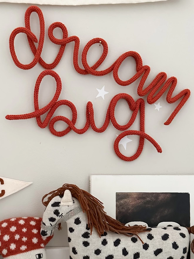 "dream big" motivational knitted wall art hanging up on a grey wall with white star stickers on it. 
