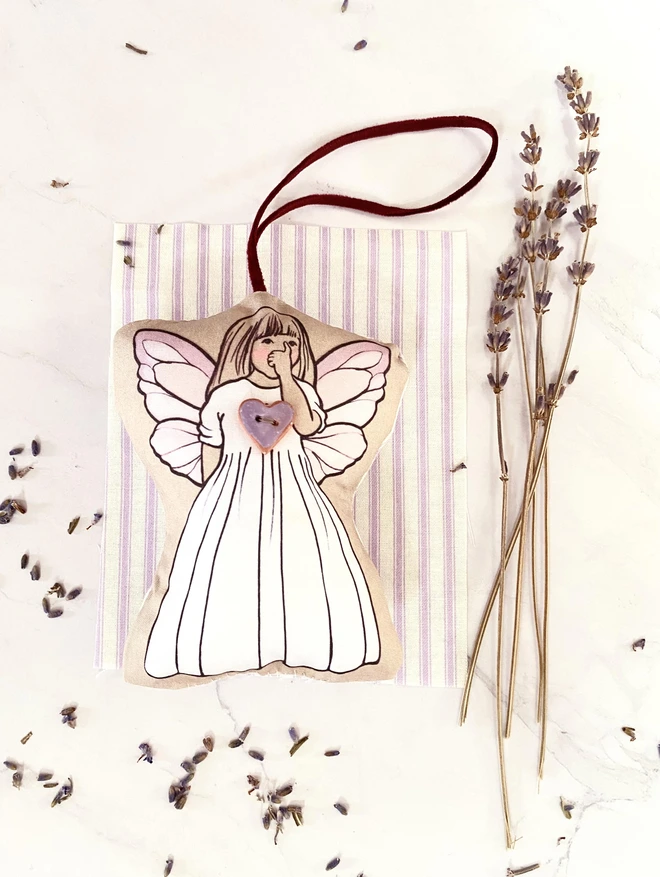 a fabric fairy decoration next to lavender on a stripped  fabric