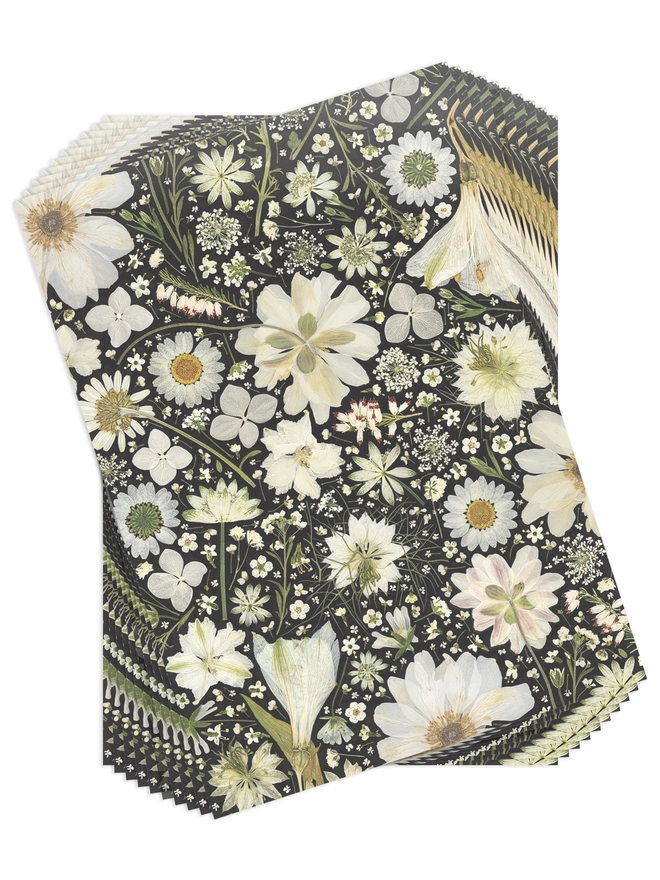 Set of 10 Folded wrapping paper sheets with a floral design created from white pressed flowers on a black background.