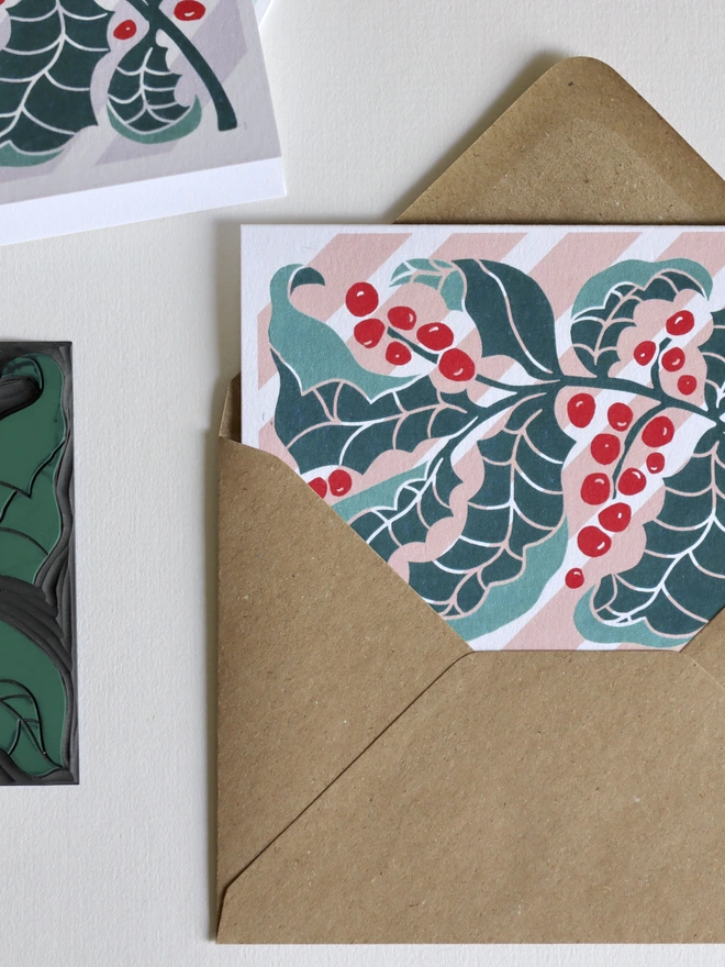 colourful linocut holly leaves greeting card on a candy striped back ground