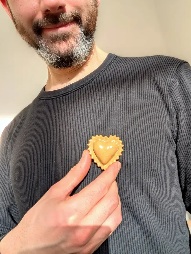 ceramic pasta pin badges. a ceramic heart-shaped ravioli badge photographed on a jumper.