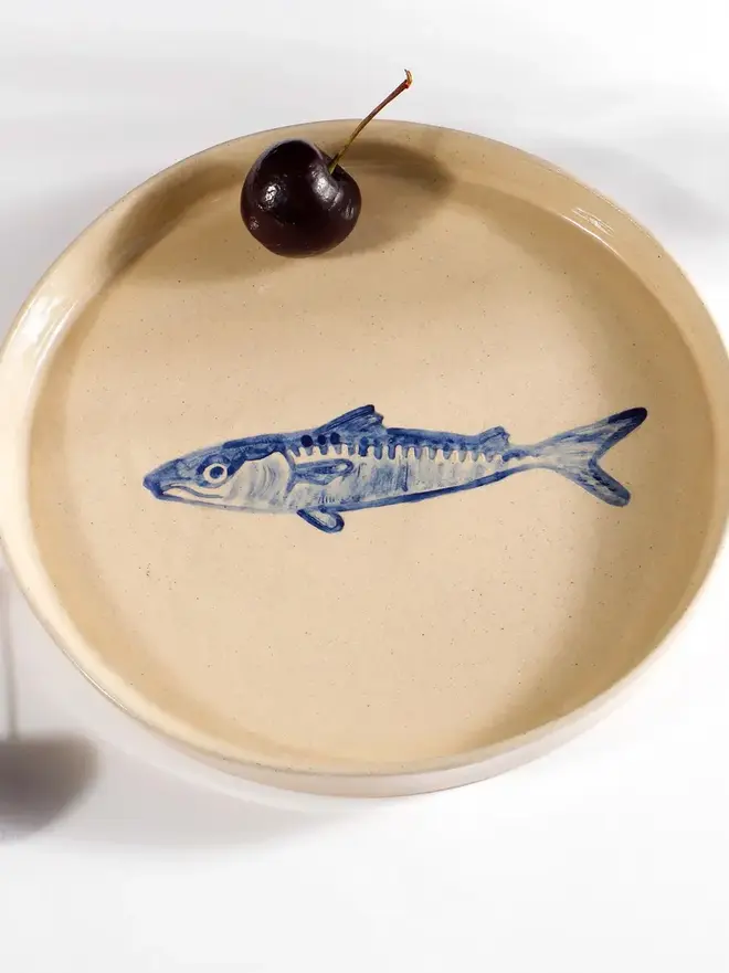 Handmade Ceramic Side Plate With Blue Fish Design, a side plate with. blue fish design sitting on a white surface with a fruit in it. 