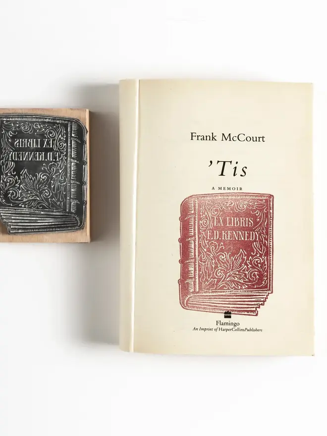 Wooden rubber stamp with an illustrated antique book design, shown next to a red ink stamped impression reading ‘Ex Libris F. D. Kennedy’.