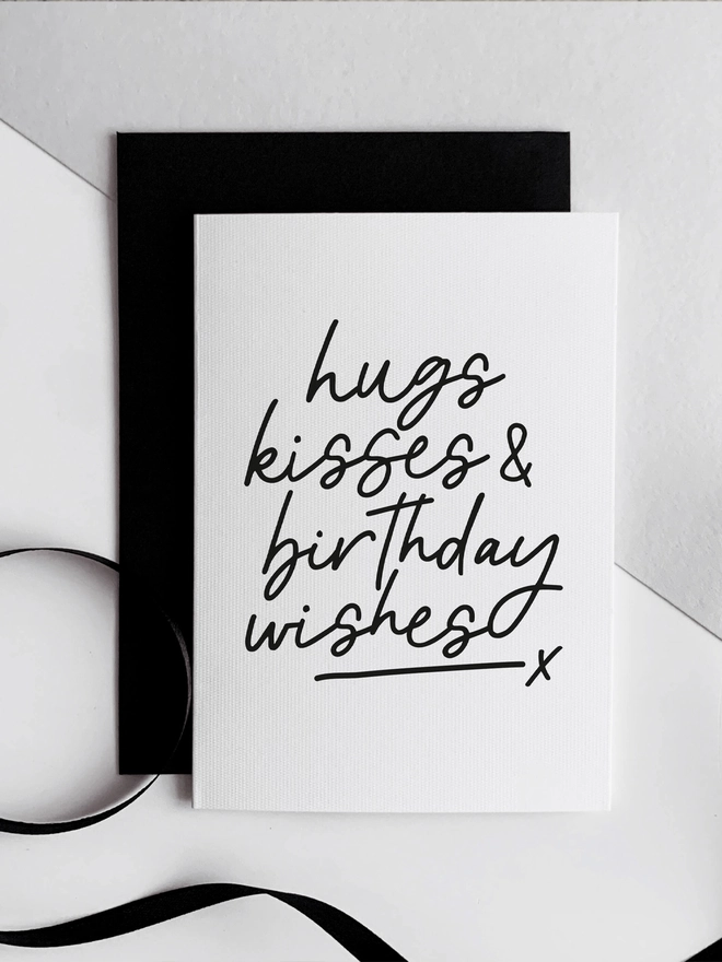 White birthday card with bold black Hugs Kisses Birthday Wishes text and black envelope