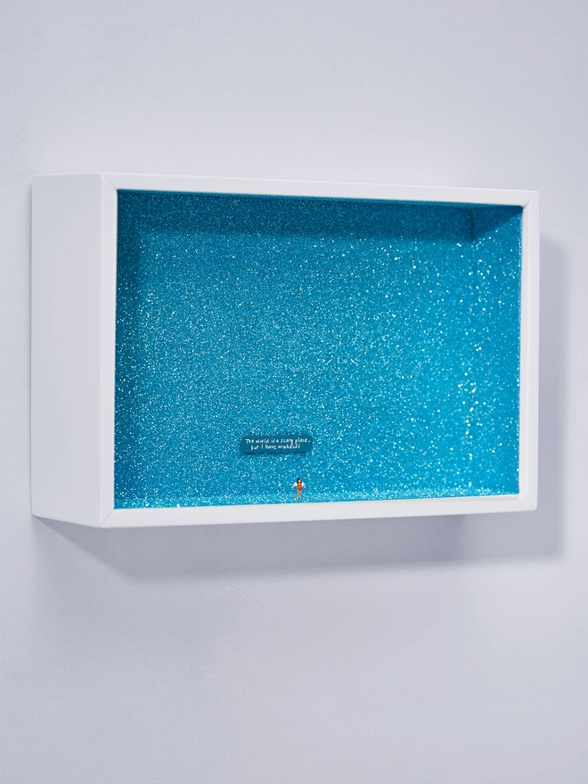 Miniature scene in an artbox showing a tiny girl in armbands against a sparkling turquoise glittery backdrop ,evoking a swimming pool. The words “The world is a scary place but I have armbands” are written on the back wall.