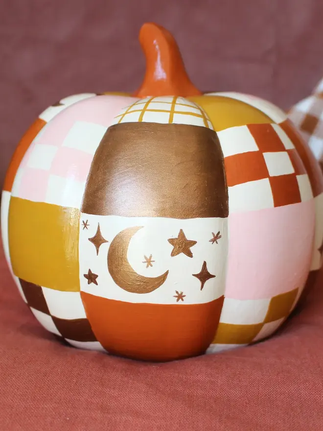 hand-painted celestial patchwork ceramic pumpkin. a ceramic pumpkin painted with patchwork colours of gold, pink, brown and stars and moons.