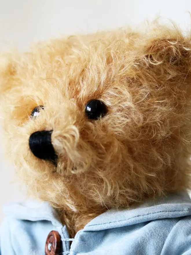 Handmade teddy bear with soft textured fur, wearing a blue jacket, posed against a plain background.