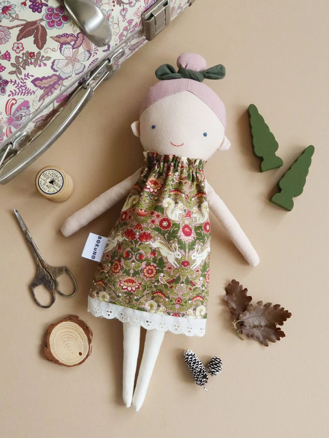 Cotton and linen doll with fair skin and pink hair, wearing william morris-esque print with animals and flowers.