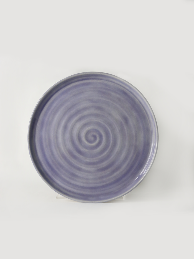 A handmade ceramic side plate in amethyst purple glaze, photographed from the front against a plain white background, showing a natural concentric swirl texture from the wheel-throwing process