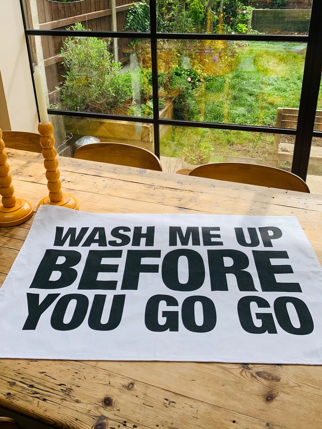 London Drying Wash Me Up Before You Go Go black screen printed text on white tea towel laying on timber kitchen table
