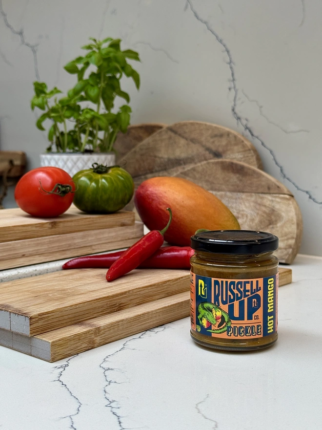 father's day pickles - spice set. a jar of  hot mango pickle photographed next to a chopping board with chillies and a mango.