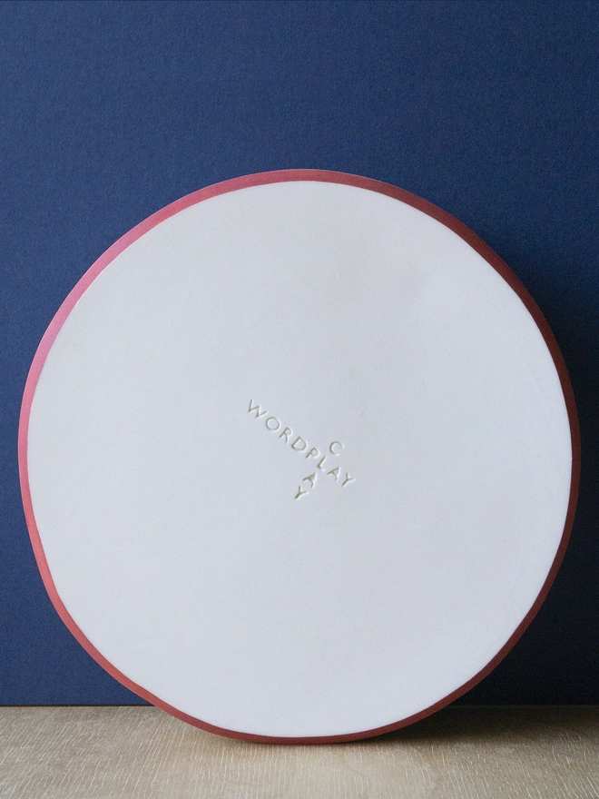 Ceramic porcelain dish with red rim and Wordplay Clay stamped into the base.