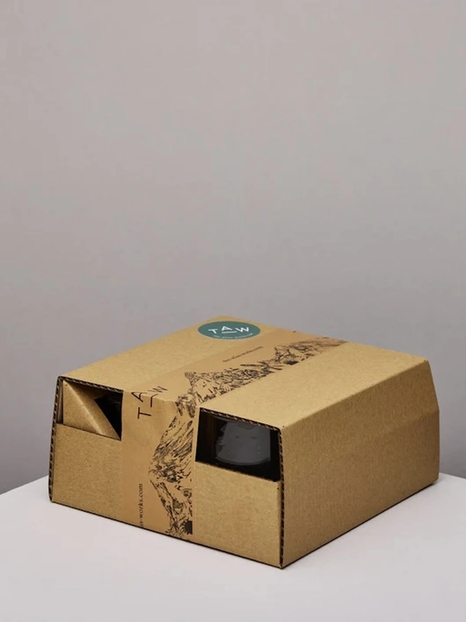 Whisky Glasses (Set Of 3), a set of whisky glasses and a jar packaged inside a cardboard box sitting on a plain counter top against a grey backdrop. 