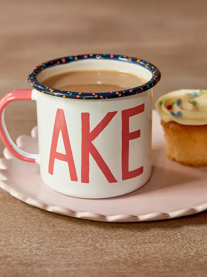 white mug with pink 'cake' text and paint splatter rim