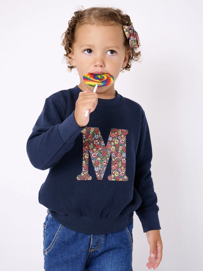 a 4 year old girl wearing a navy sweatshirt with her initial personalised in floral liberty print on the front