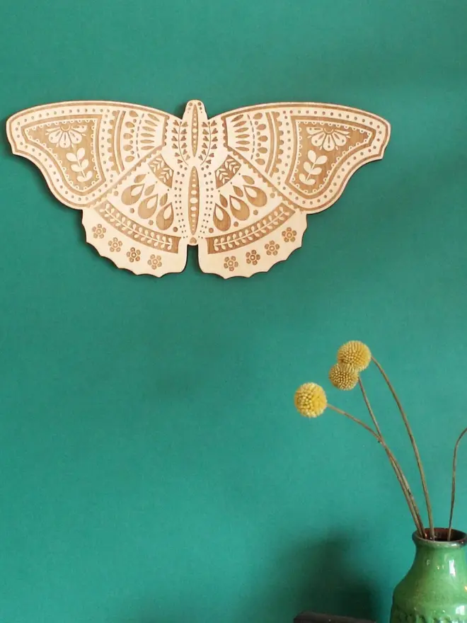 Wooden Folk Art Butterfly Hanging Decoration, wooden insect decoration hanging on a green wall. 