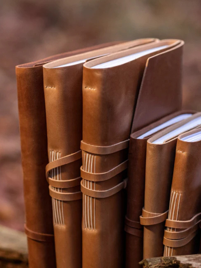 leather refillable ring binder. a line of light brown leather journals lined up against each other.
