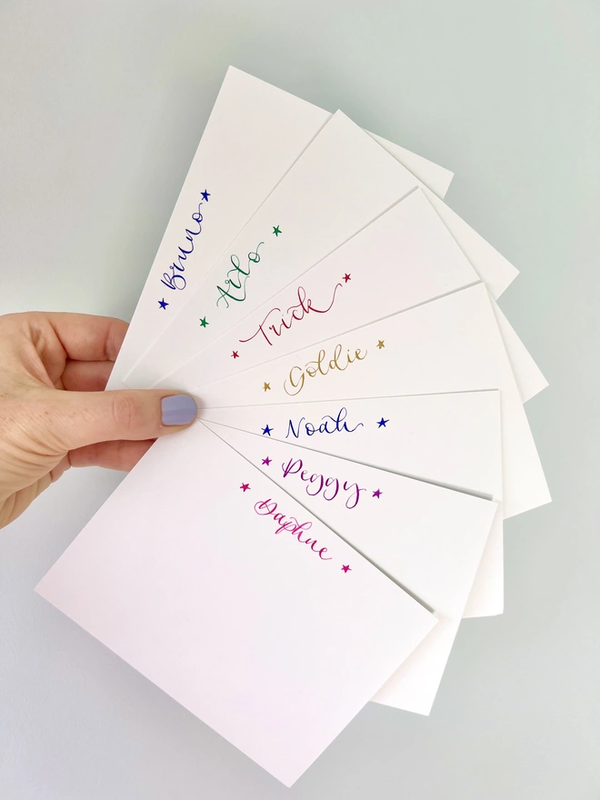 A selection of notecards with different names handwritten in calligraphy and bookended by singular stars at the top of each card. 