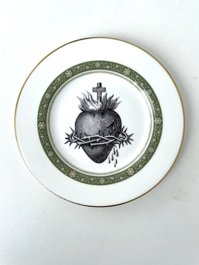 a vintage plate with a white and gold ornate border, the centre is lemon yellow and printed on that is a black illustration of a sacred heart