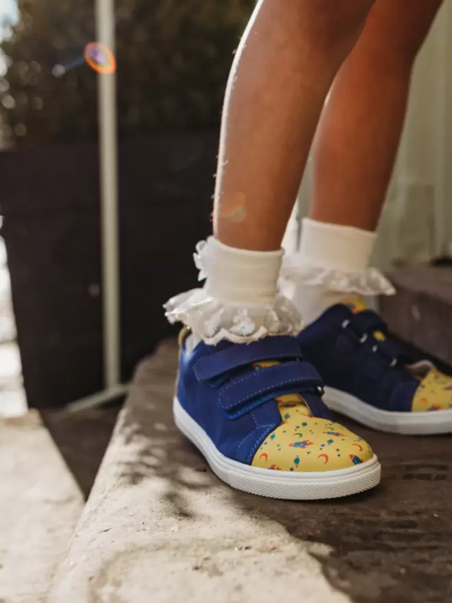 Little girl with white frilly socks and Pip and Henry blue and h=yellow space print sneaker