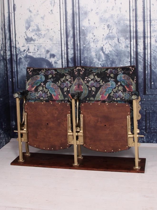A set of two vintage cinema seats upholstered in a black peacock velvet with both seats closed, against a blue marbled wall