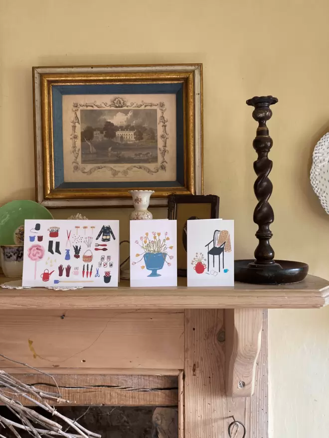 3 greetings cards sat on a wooden fireplace surrounded by antiques. 