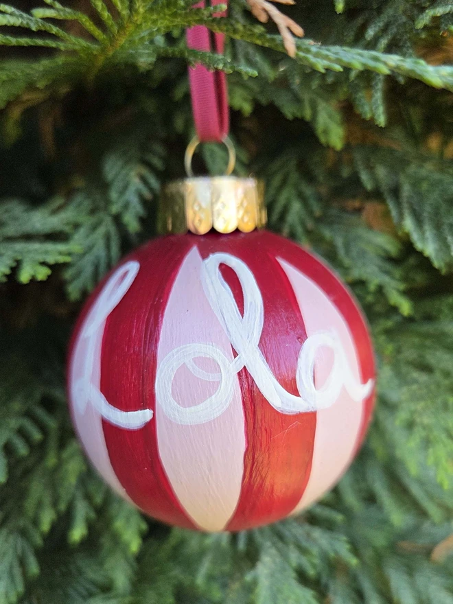 hand painted pink and red stripe bauble with name personalisation, hanging on a christmas tree