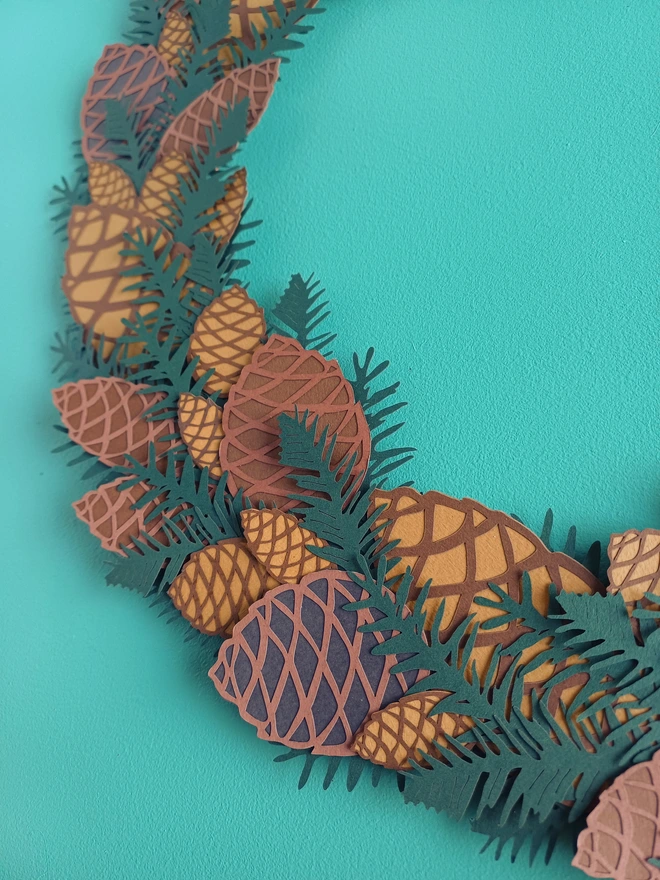 Closeup showing three different size and tone of papercut pinecone in papercut wreath