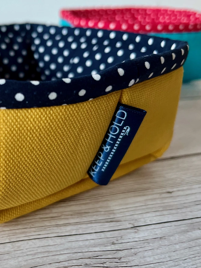 Close-up of a yellow fabric storage basket showing the navy Keep & Hold logo label.