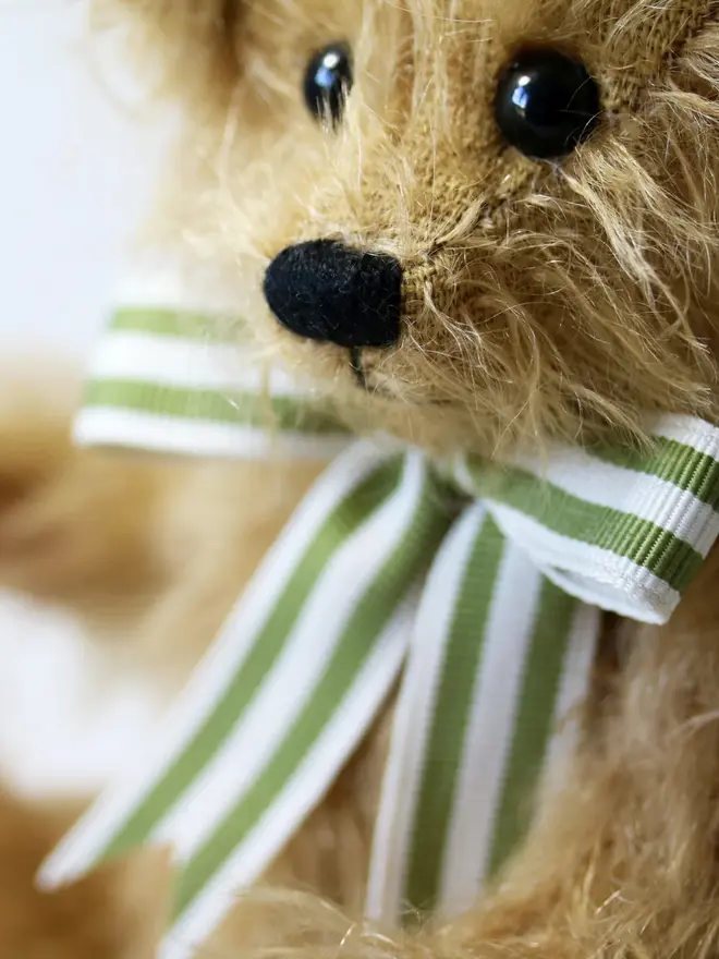 Handmade brown teddy bear sitting upright with a green striped ribbon bow against a plain background.