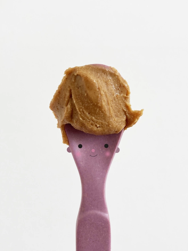 A purple spoon with a cute face and peanut butter for hair  