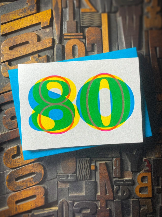Handmade letterpress 80th birthday card featuring bold overlapping numerals printed in vibrant fluorescent cyan, magenta and yellow inks. Each card is individually hand printed using traditional letterpress techniques on luxury paper stock, creating a beautifully tactile finish with a subtle deboss and rich layered colours inspired by the CMYK printing process.