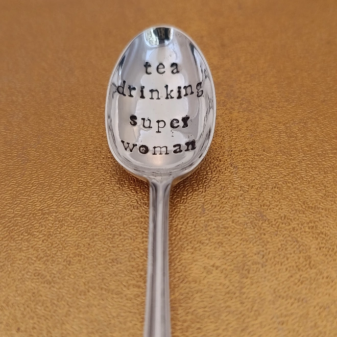 Teaspoon on gold background stamped with tea drinking super woman