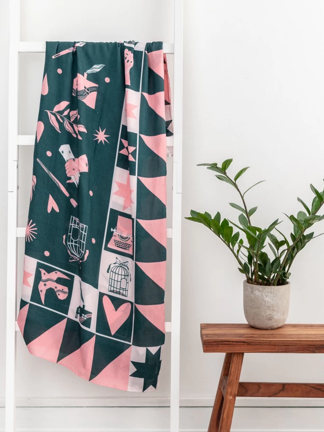 A large light weight forest green and calamine scarf displaying a range of motifs representing iconic women hanging from a rail