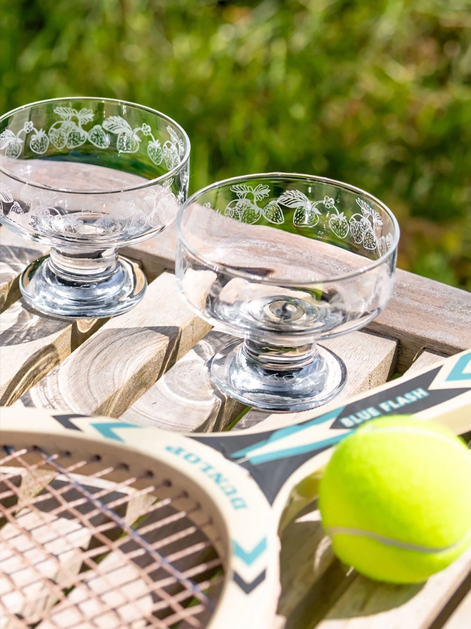 Strawberry design glass dessert bowls on wooden table with vintage tennis racket and ball