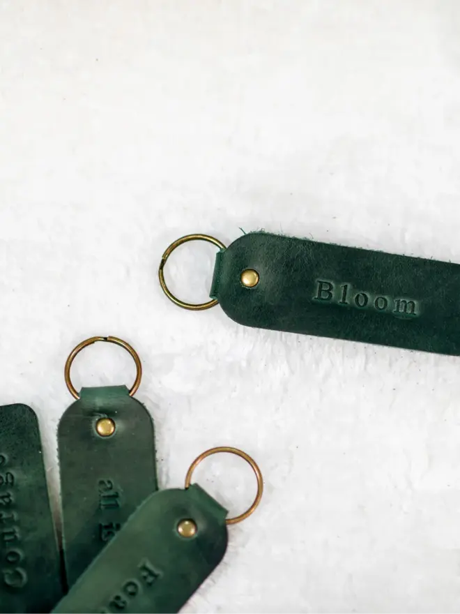 custom leather embossed keyring. dark green leather keyrings embossed with 'bloom' photographed against a white background.