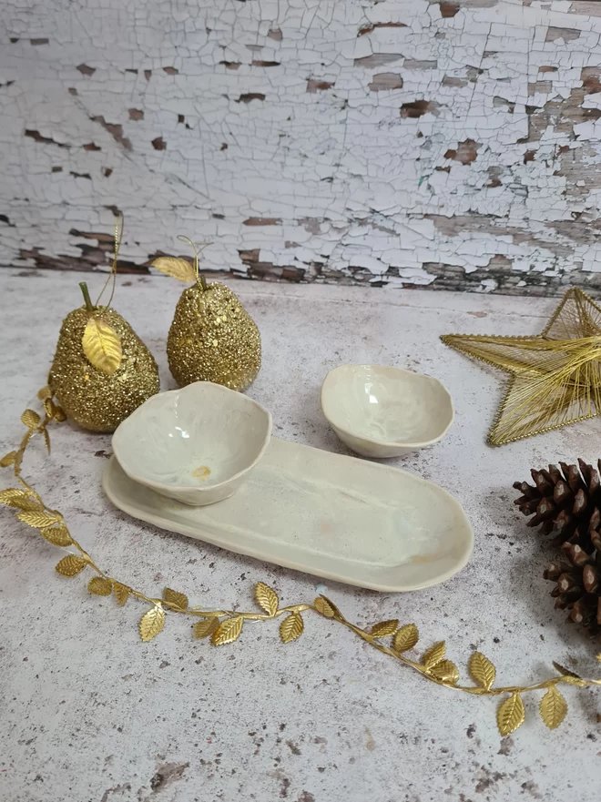 Serveware, Small serving dish crafted from stoneware clay and glazed in Dream Catcher glaze with creams, whites, hints of pink, lilac and specks of metallic gold. Two bowls and an oval dish, tapas dish, snack dish, gift, handmade, homeware, cream background with gold leaves and christmas decorations