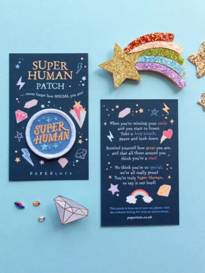 The front and back of the navy patch card, decorated with gems, stars and lightning bolts. The back has an uplifting poem reminding children they're truly Super Human.