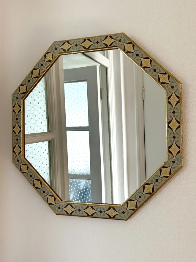 Medium sized octagonal wall mirror with a hand painted decorated frame with gold stars and blue star burst repeating pattern around the frame