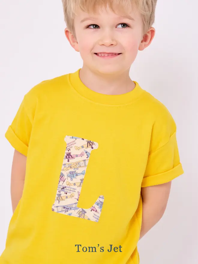 a 4 year old boy wearing a yellow t-shirt with a Liberty initial letter on front