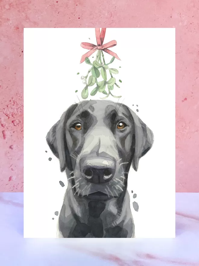 A Christmas card featuring a hand painted design of a Black Lab, stood upright on a marble surface.