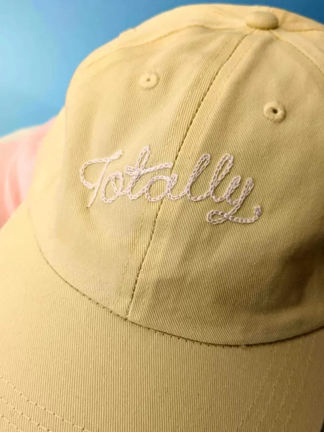 Yellow relaxed style adult cap with white embroidery reading 'Totally' on a blue background