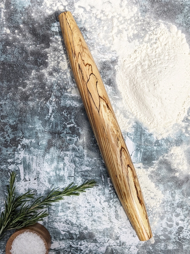 A stunning hand made rolling pin in Spalted Beech by Something From The Turnery. The rolling pin sits on an art house kitchen top amongst flour, rosemary and a wooden salt pot, prepped to bake some delicious bread!