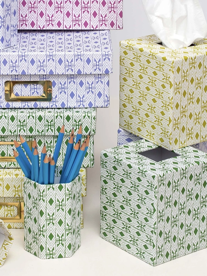 Tijan Tissue Box Cover, a colourful tissue box sitting on a desk. It is accompanied by other desk accessories. 