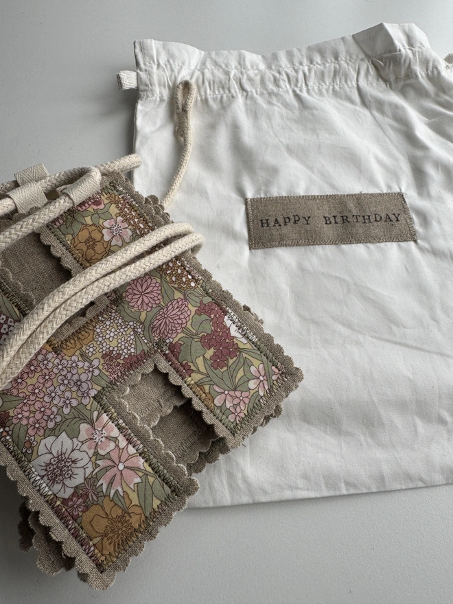 A fabric letter garland with pink and green florals tied with string on a white bag with Happy Birthday label on