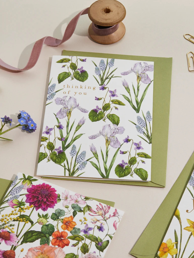 'thinking of you' illustrated floral card. a white floral card and green envelope photographed against a white background.