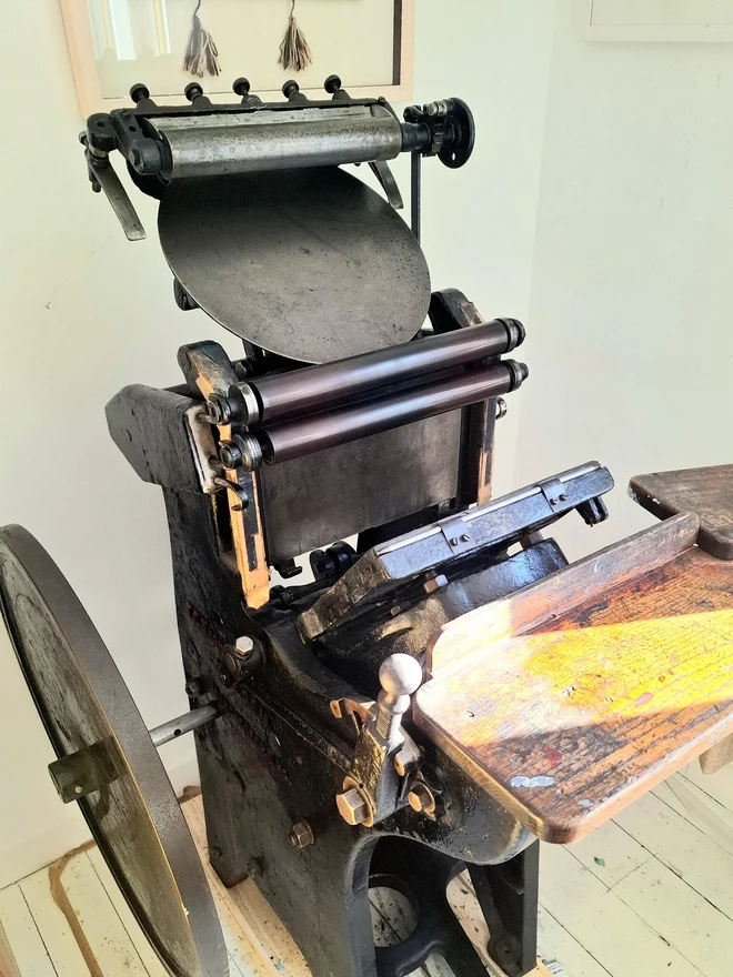 'Good Luck' Letterpress Handprinted Greetings Card, the card being made by the machine in a studio on a wooden surface. 