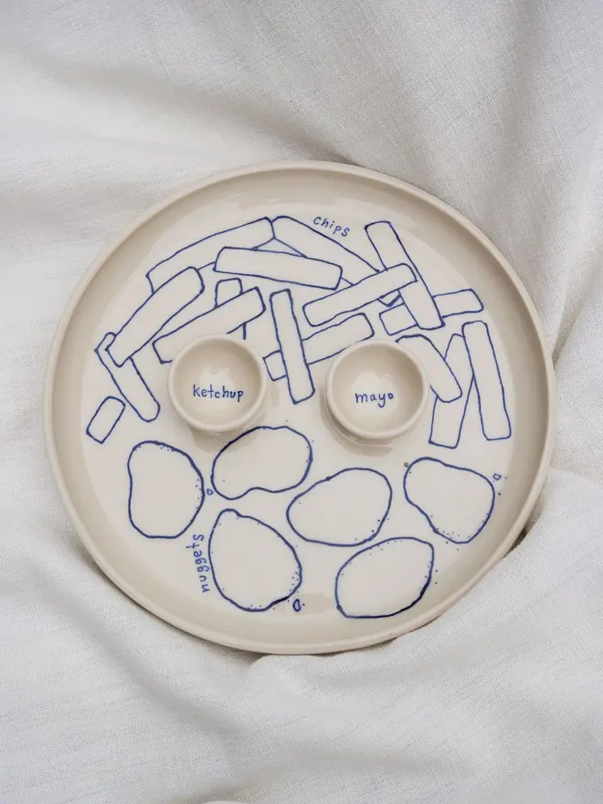 Dippy Chips & Nuggets Dinner Plate, a white dip dinner plate with blue outlines for nuggets and chips sitting on a white bed cloth. 